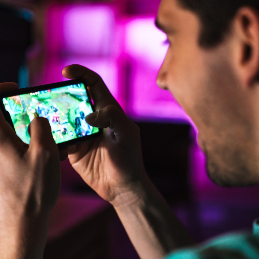 Image closeup of smiling man playing video game on mobile phone