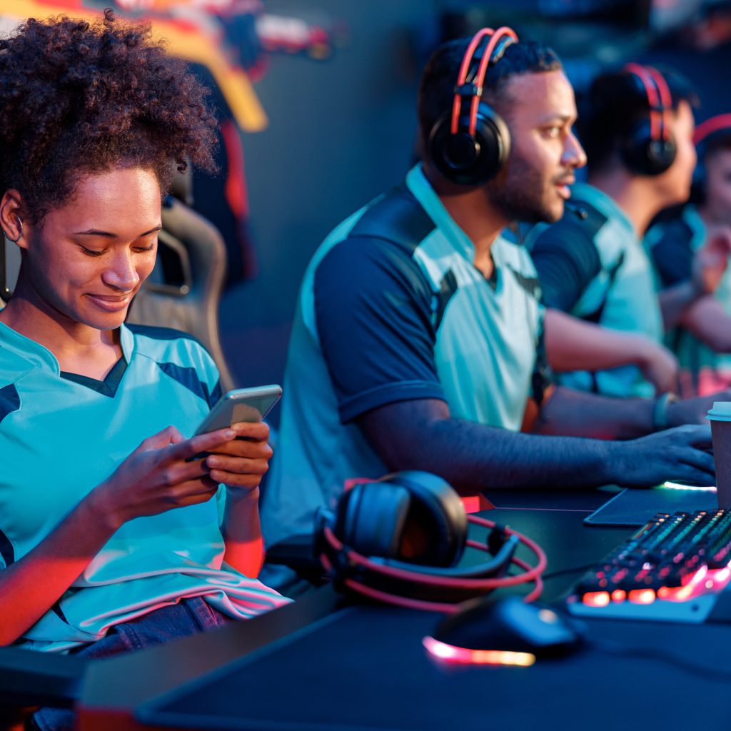 Cute female cybersport gamer sitting in gaming chair and playing mobile game on cellphone in computer club