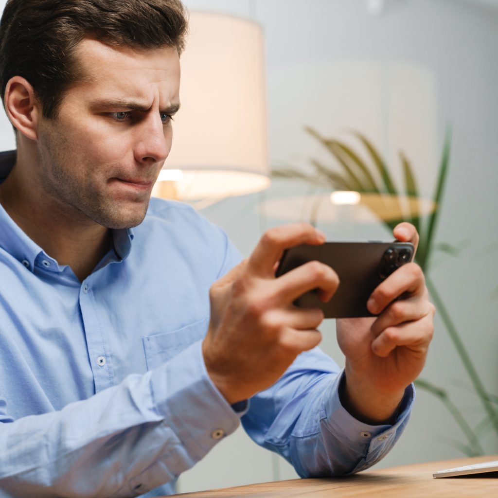 Confused frustrated male manager looking at mobile phone while sitting at the desk