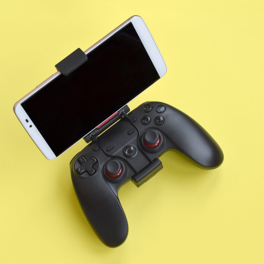 Modern black gamepad for smartphone on yellow background close up. Mobile video gaming device