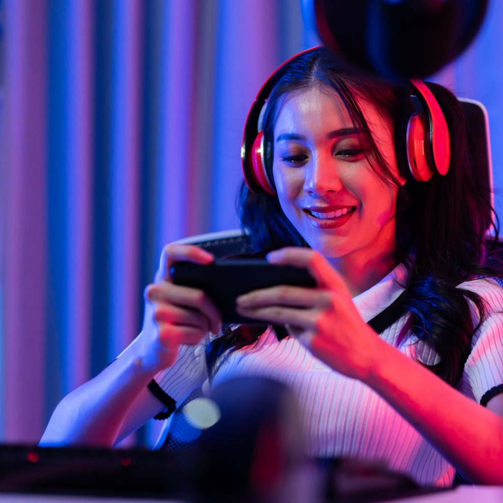 Asian young beautiful woman playing mobile game on smartphone at home. Attractive casual girl feel happy and relax sit on chair having fun touching screen on phone to play video enjoy victory in house